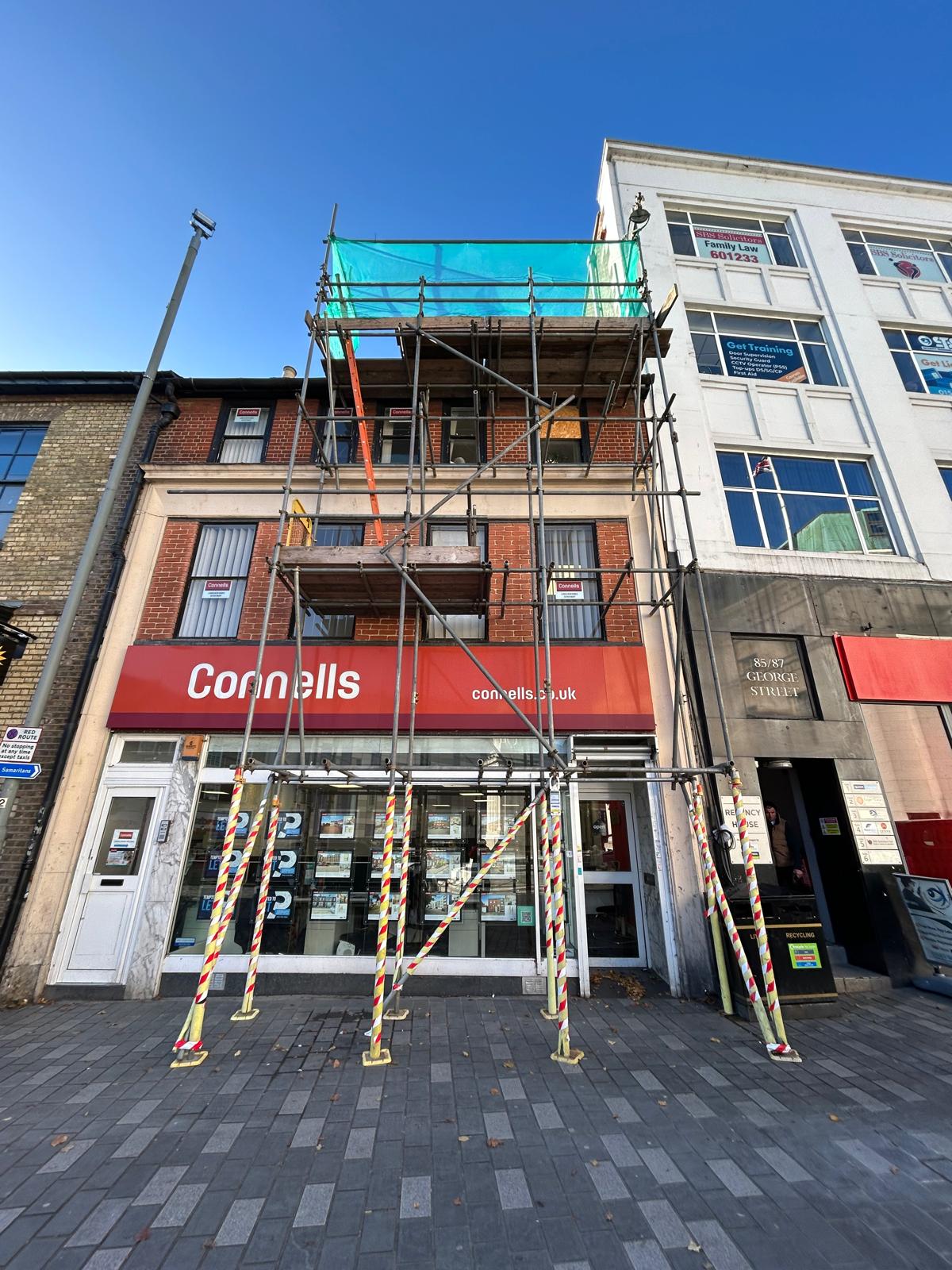 Scaffolding above a high-street shopfront beneath blue sky