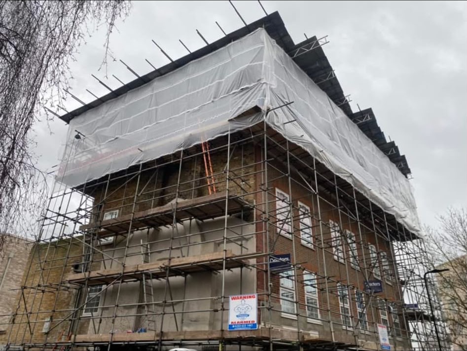 Scaffolding and white sheeting around a corner brick building